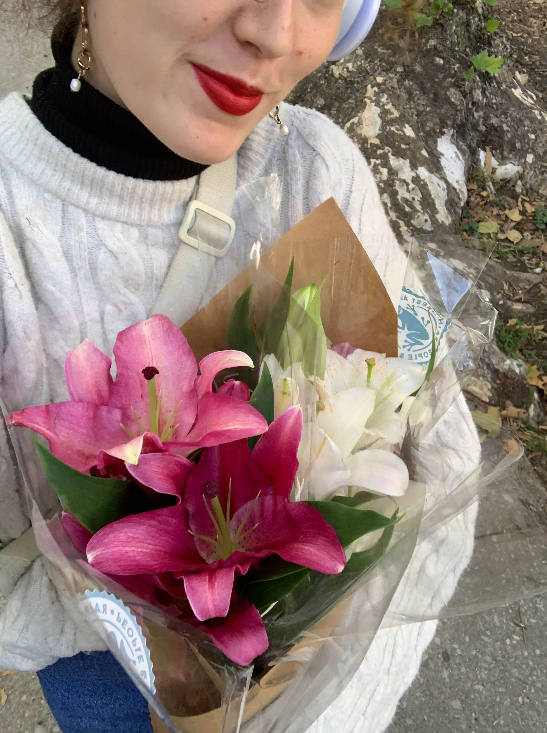 Una dona amb els llavis pintats de vermell sosté un ram de lliris rosats i blancs embolicat amb paper.