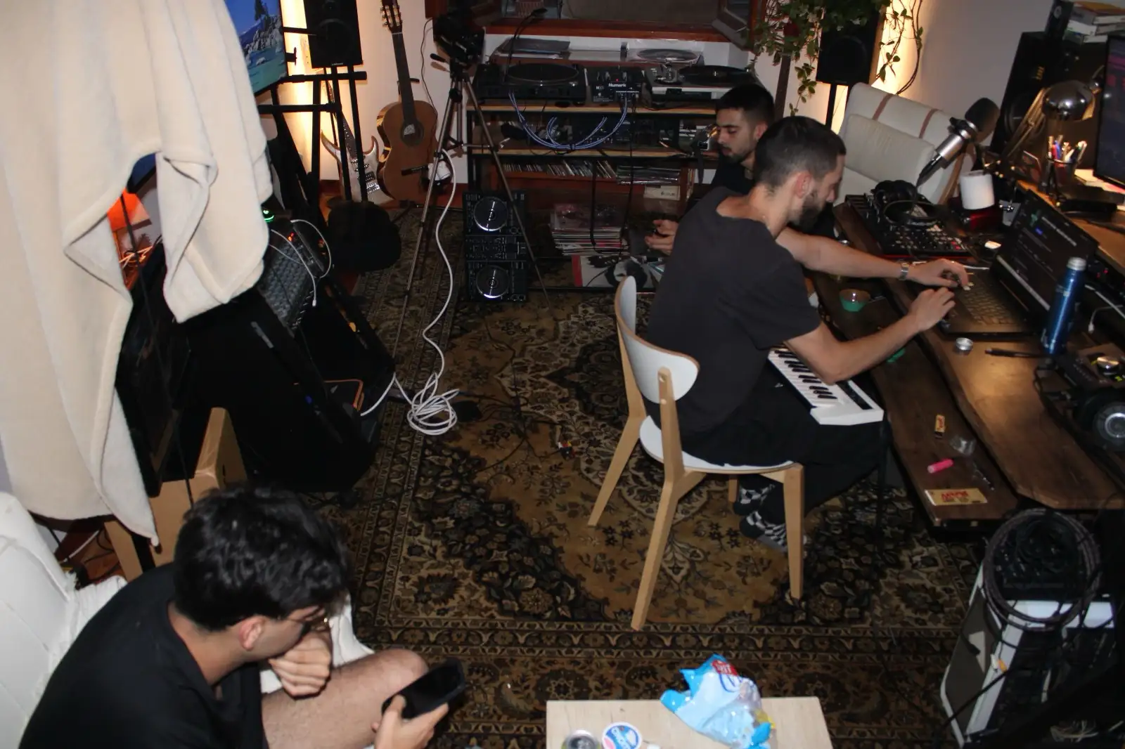 Dos joves treballen amb un teclat MIDI i un ordinador en un estudi casolà ple d'instruments i vinils.