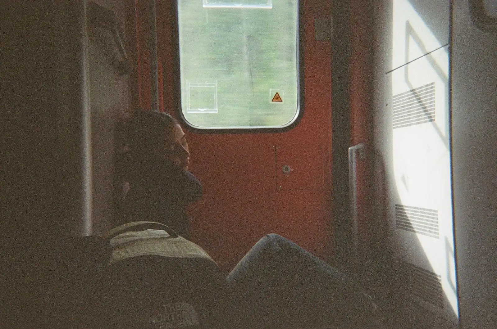 Fotografia analògica d'una persona asseguda en un tren mirant per la finestra, amb gra i llum suau.