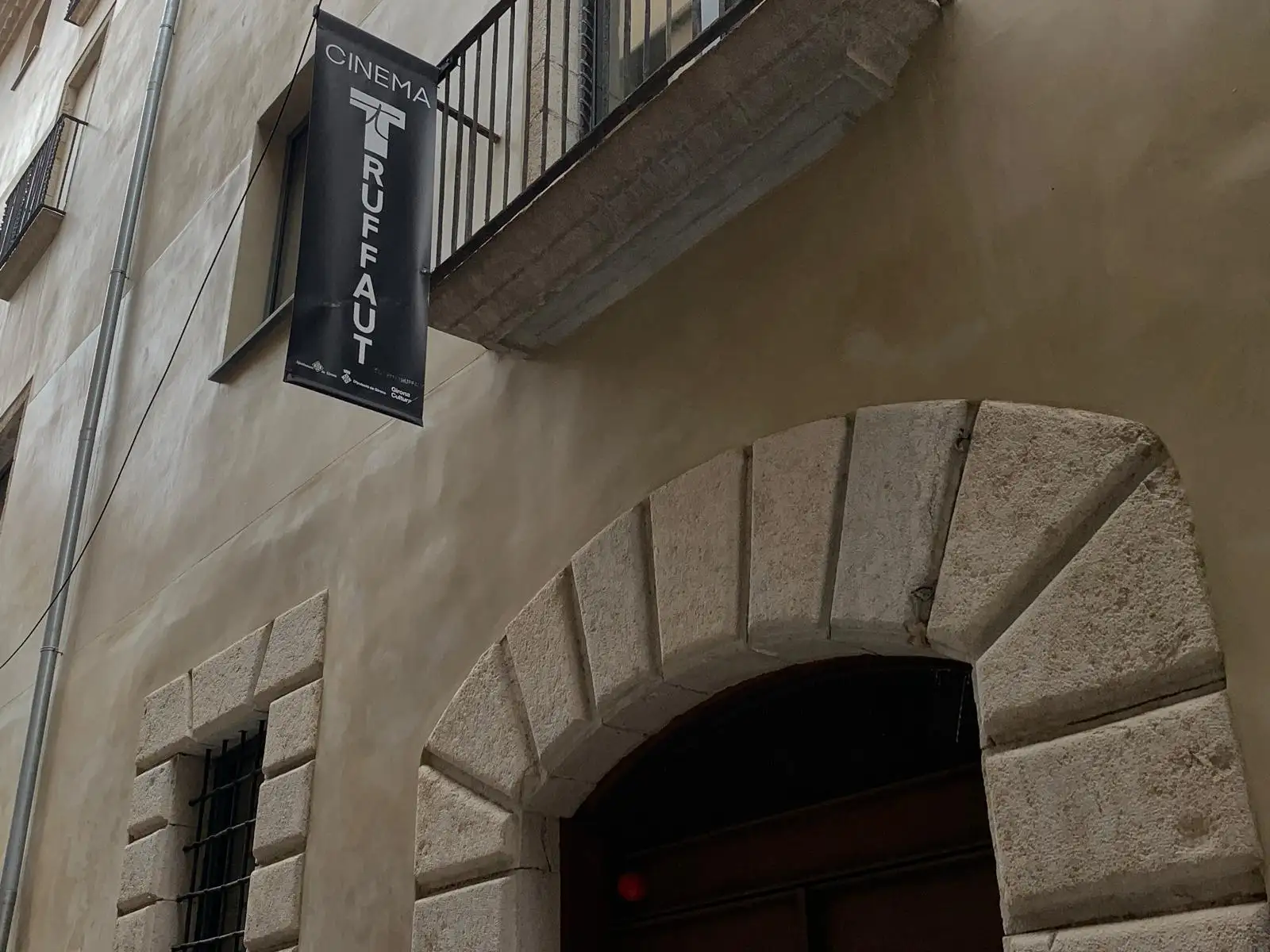 Rètol vertical del Cinema Truffaut penjat a la façana d'un edifici de pedra del casc antic.