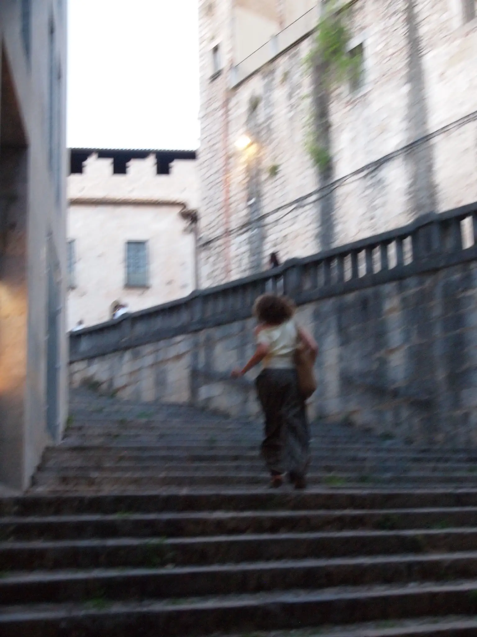 Una persona puja sola una escalinata de pedra d'un carrer antic, fotografiada de mitja esquena i moguda.